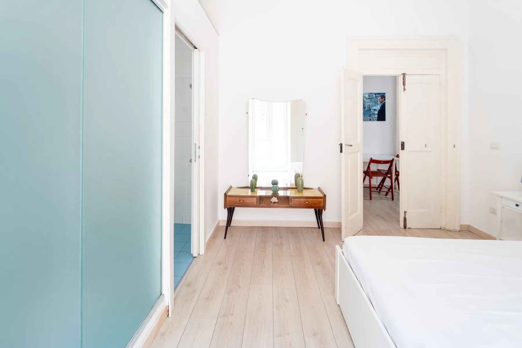 Un dormitorio luminoso con una cama, una consola de madera y una puerta abierta.