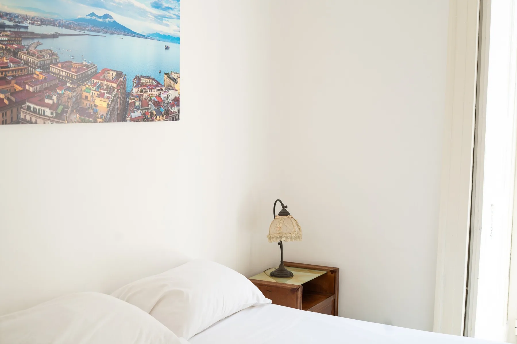 Un dormitorio con ropa de cama blanca y una mesita de madera bajo un cuadro.