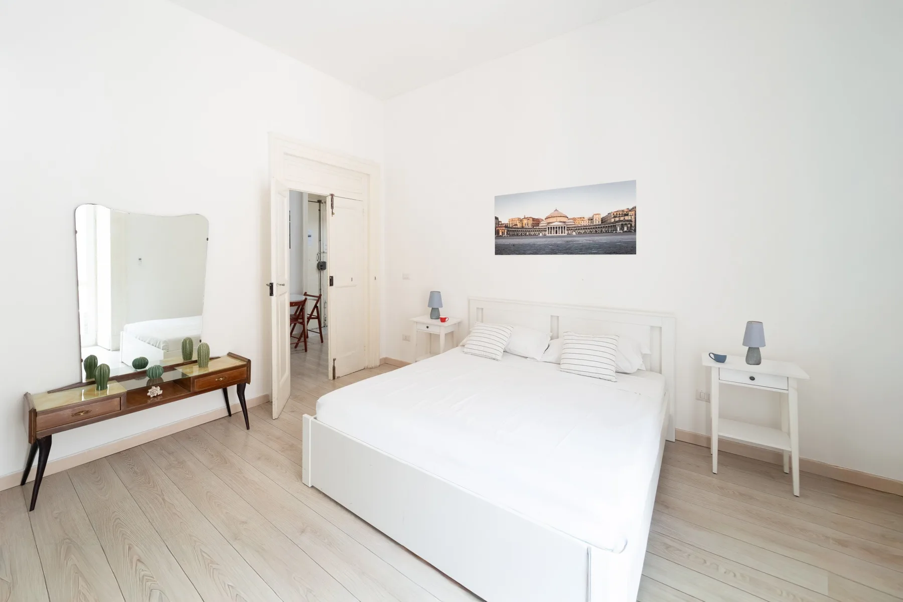 Un dormitorio luminoso con una cama blanca y un espejo sobre una consola.
