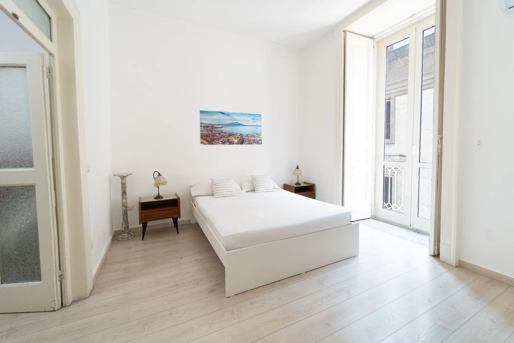 Un dormitorio luminoso con una cama y ventanas altas que dan a un balcón.