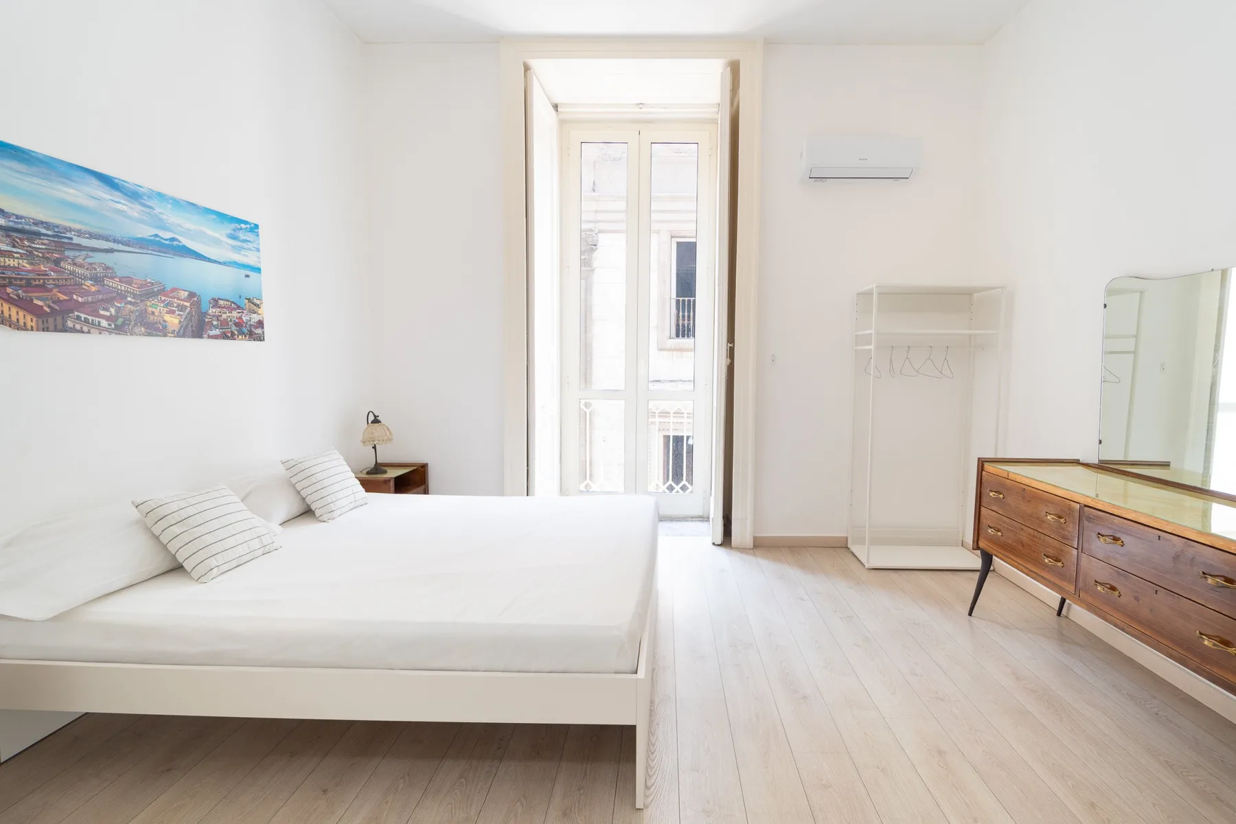 Dormitorio luminoso con cama, cómoda y puertas altas de vidrio.