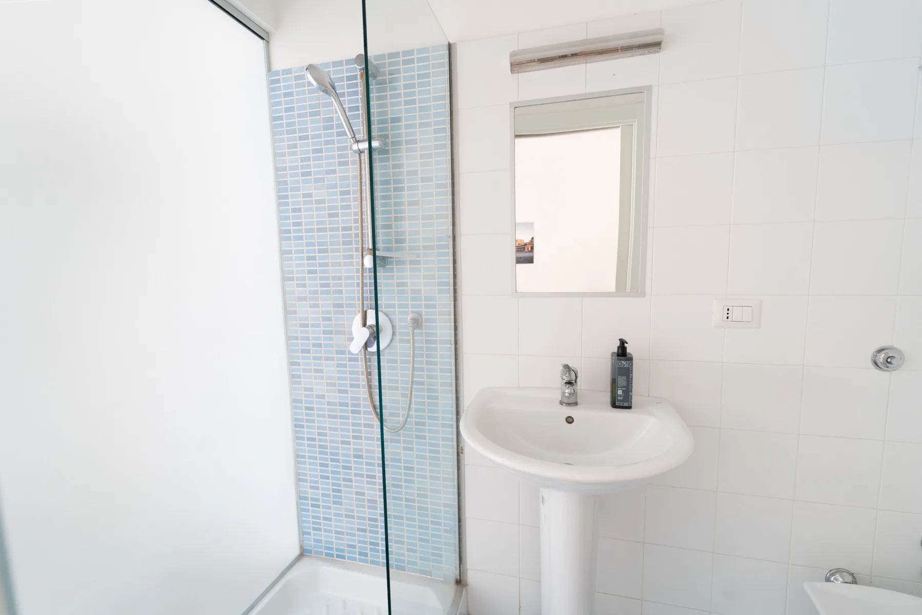 Un baño luminoso con ducha, azulejos azules y lavabo.