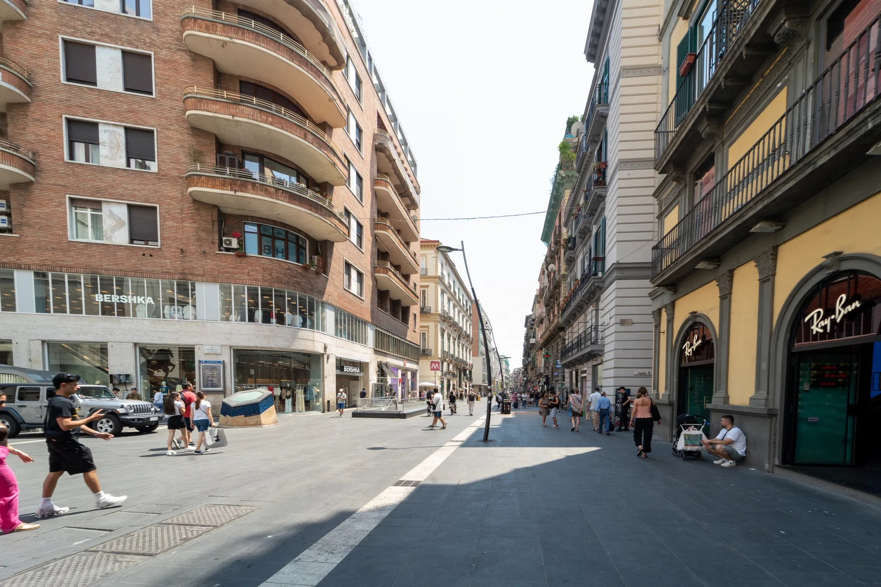 Una calle urbana flanqueada por edificios de varias plantas, tiendas y peatones.