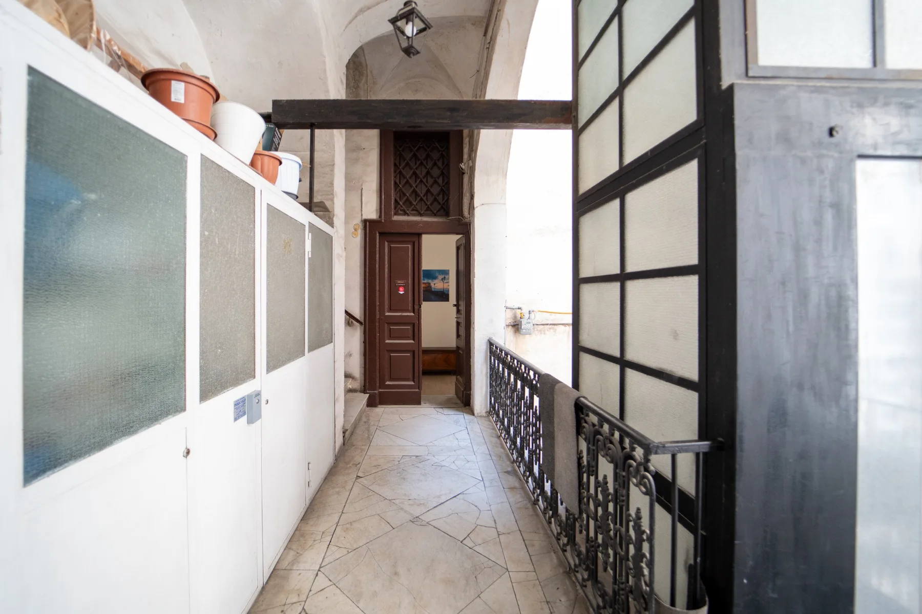 Un pasillo interior estrecho con suelo de baldosas claras y una barandilla decorativa.