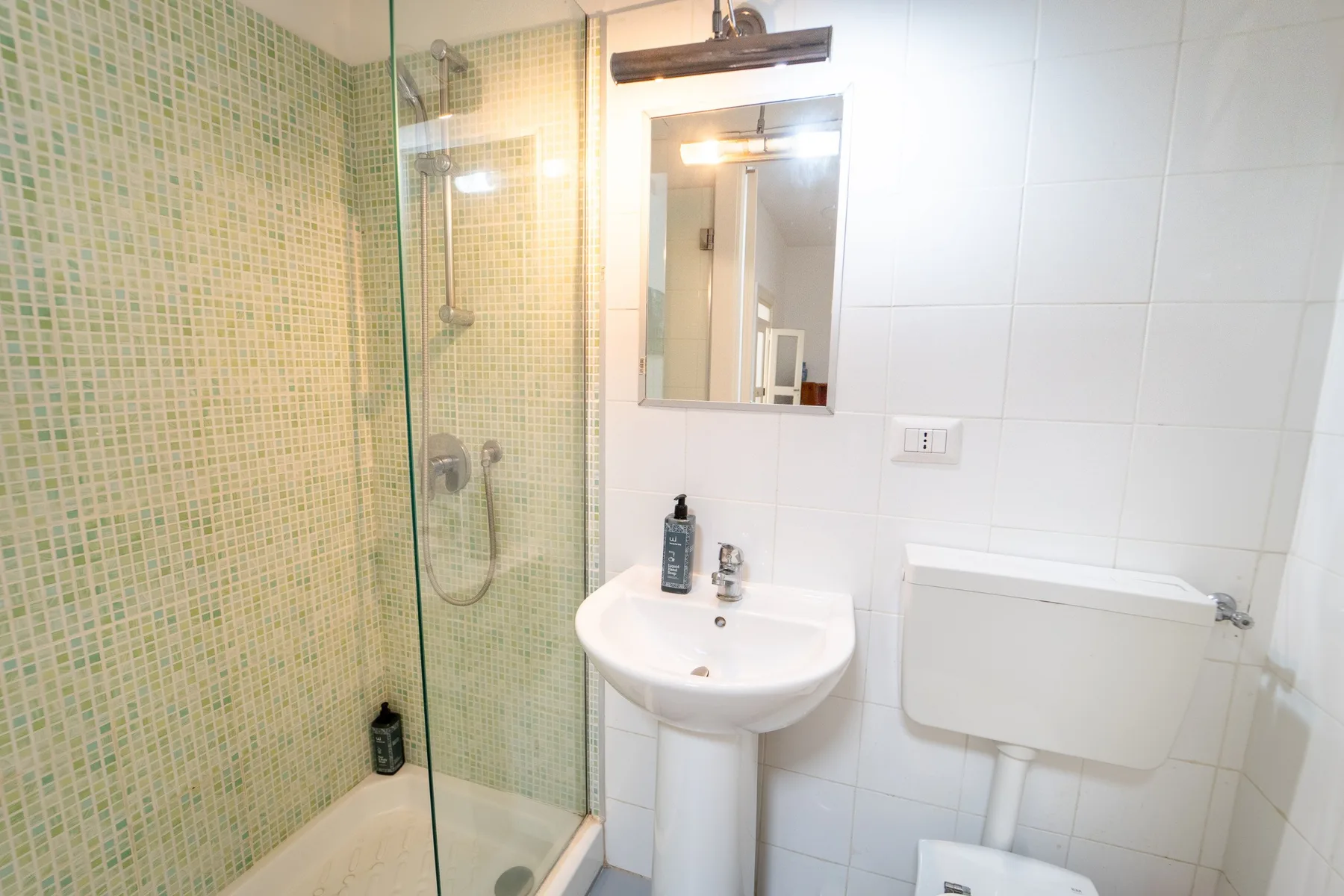 Un baño con ducha, lavabo y espejo de pared.