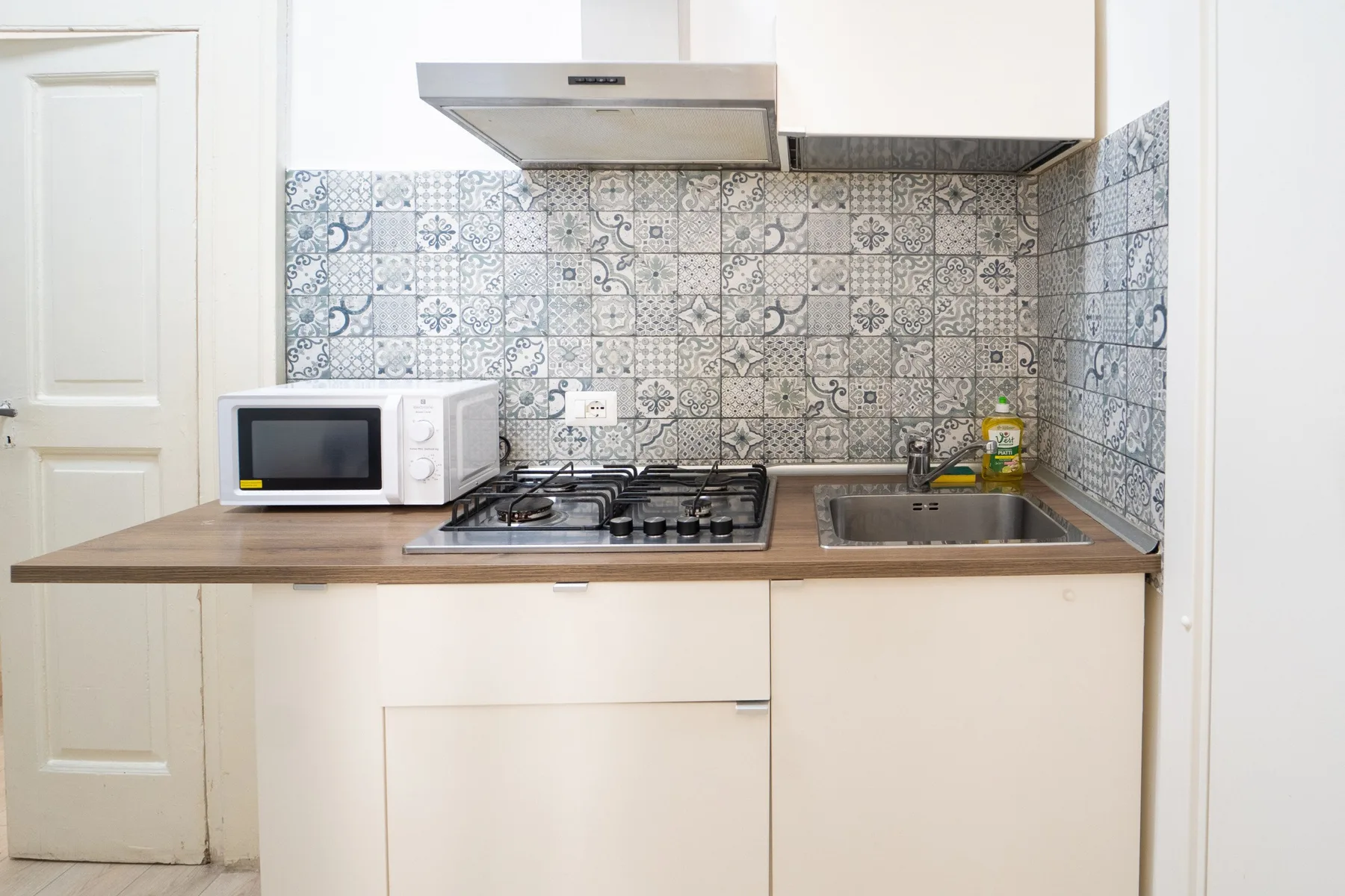 Una cocina compacta con microondas, estufa y fregadero bajo azulejos estampados.