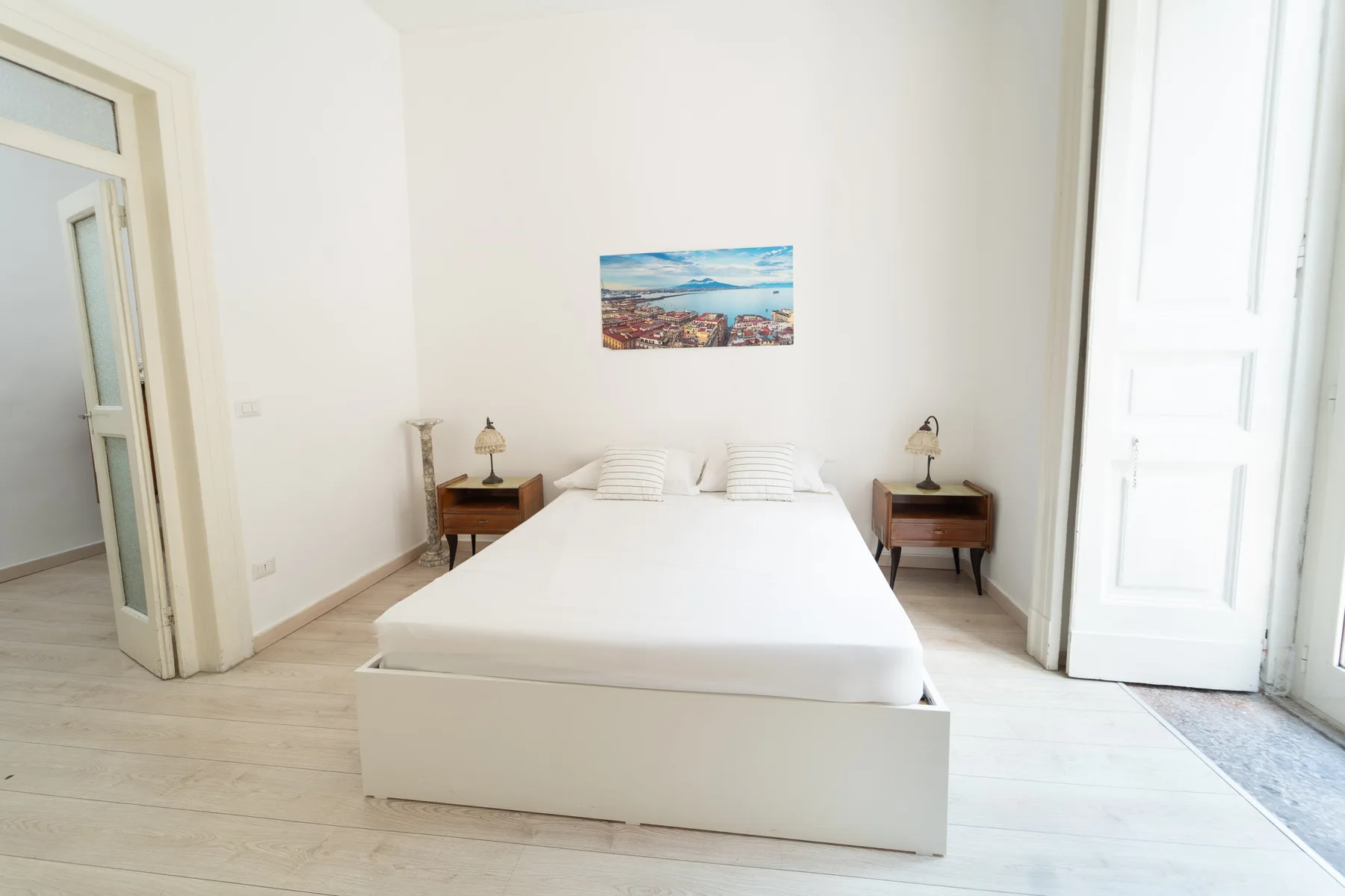 Un dormitorio luminoso con una cama blanca y mesitas de noche a juego.