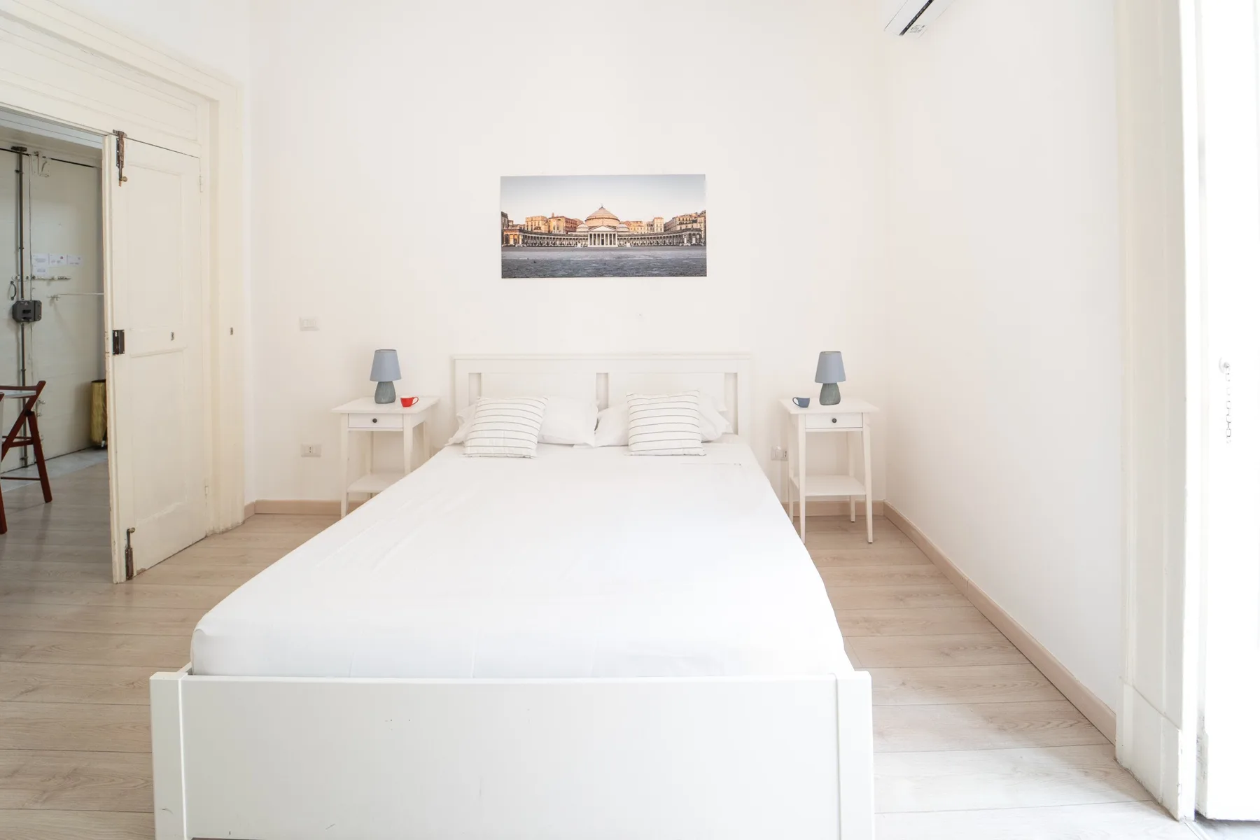 Un dormitorio luminoso con una cama blanca y mesitas de noche a juego.