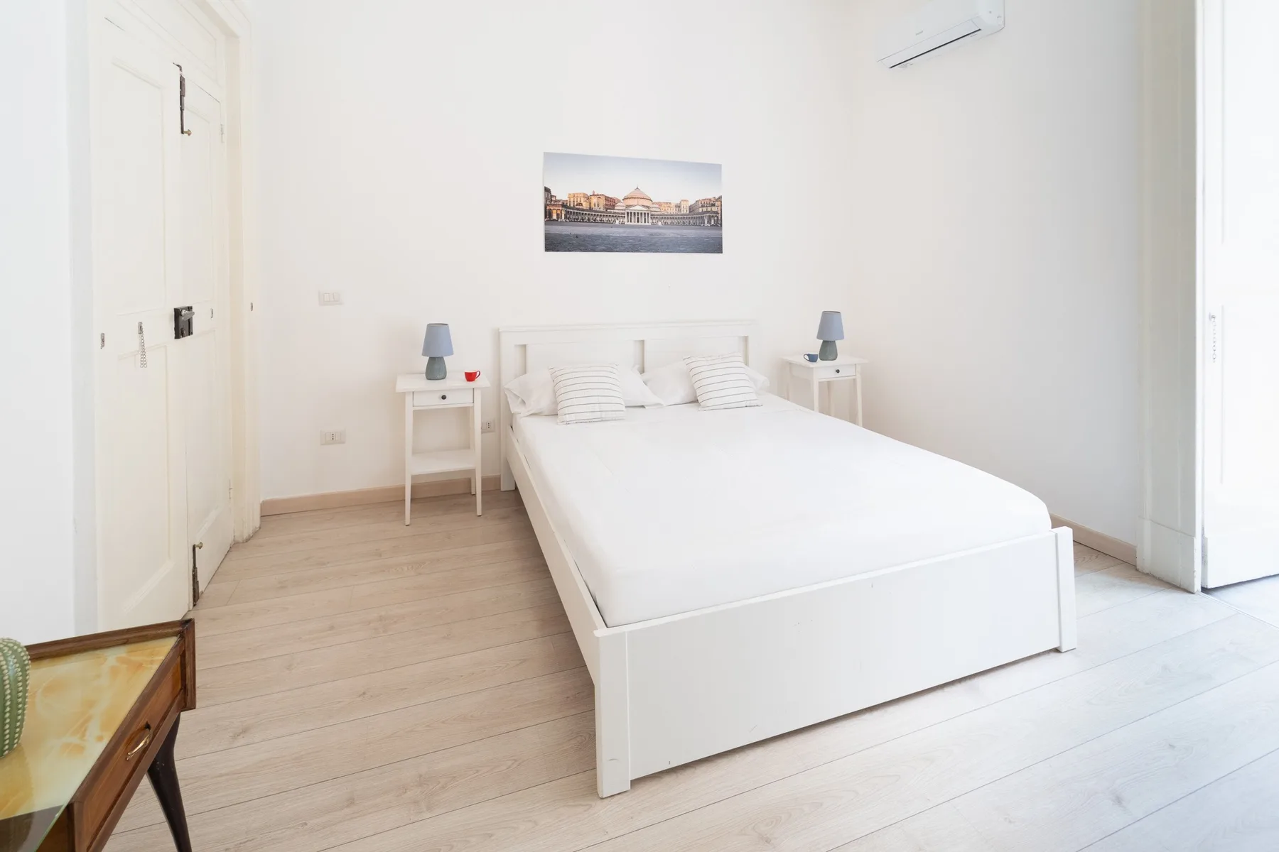 Un dormitorio luminoso tiene una cama blanca y mesitas de noche a juego.