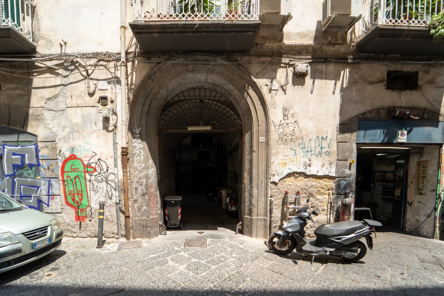 Una calle con una entrada arqueada a un edificio y scooters estacionados.