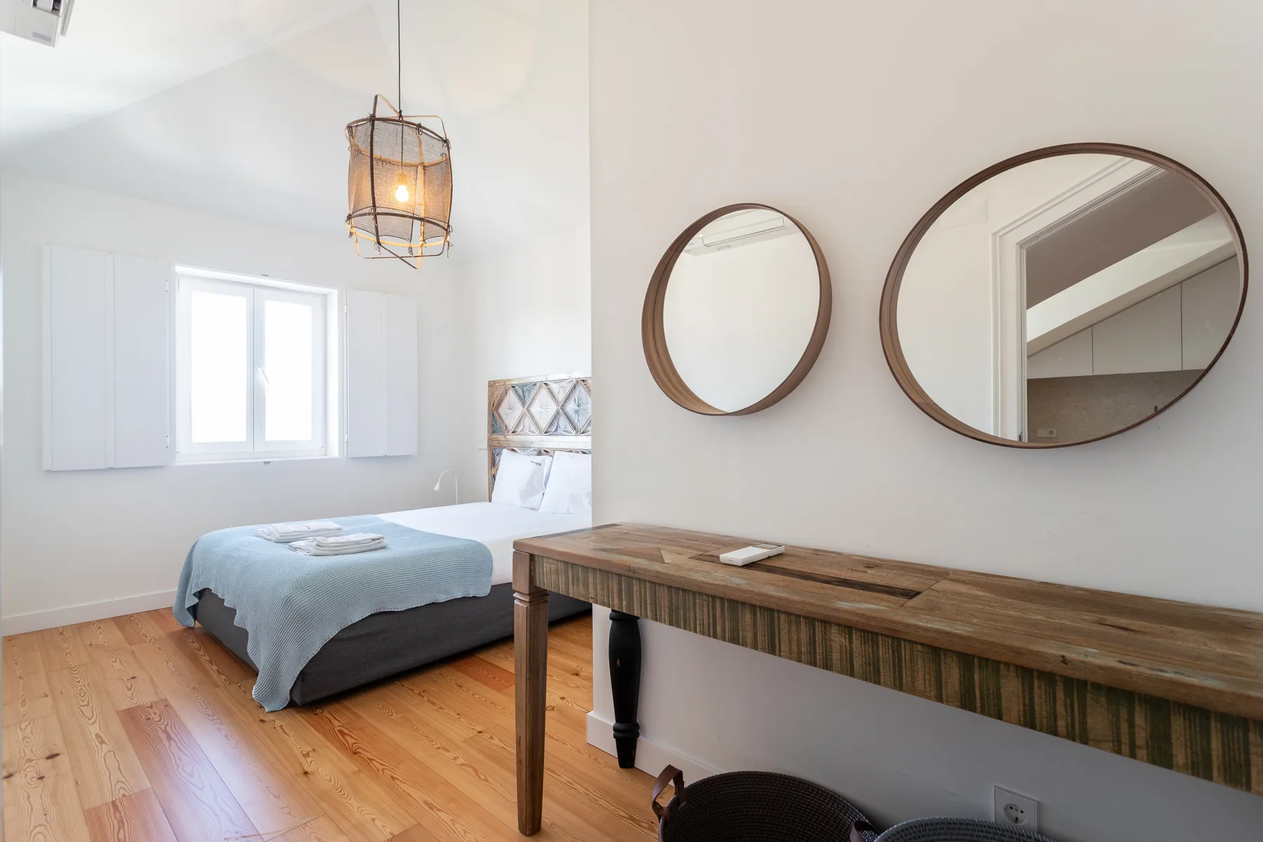 A bright bedroom with a bed, a wooden table, and two wall mirrors.
