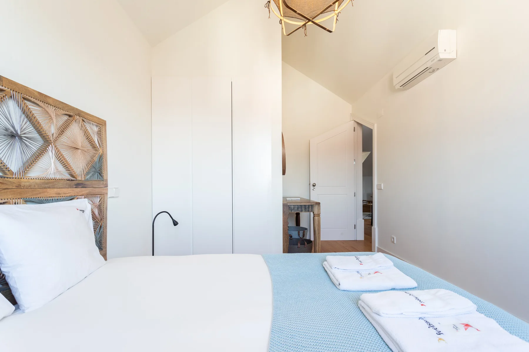 A bright bedroom with a bed, folded towels, and an open doorway.