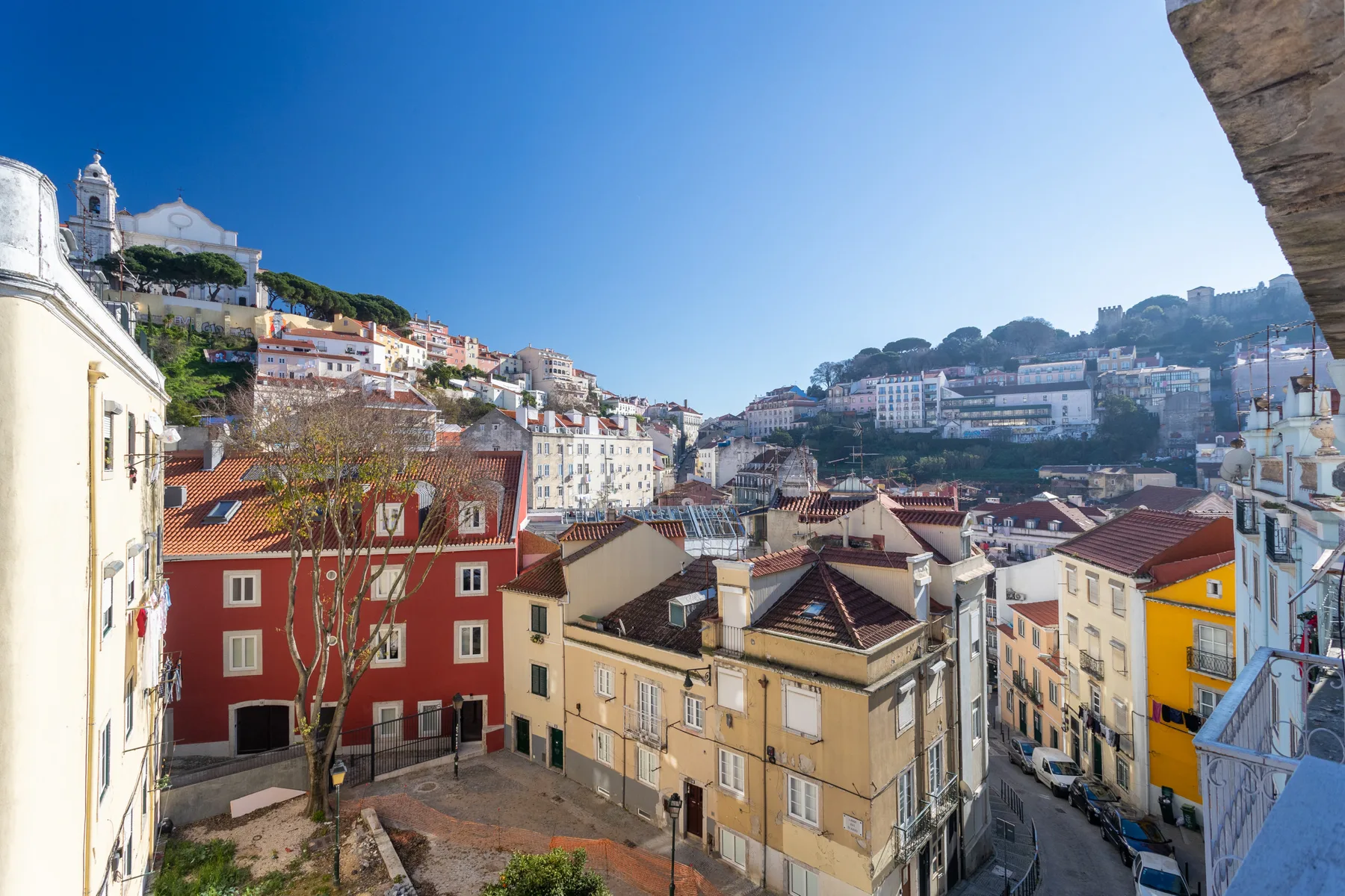 A cityscape of Lisbon's hillside buildings beneath a clear blue sky.