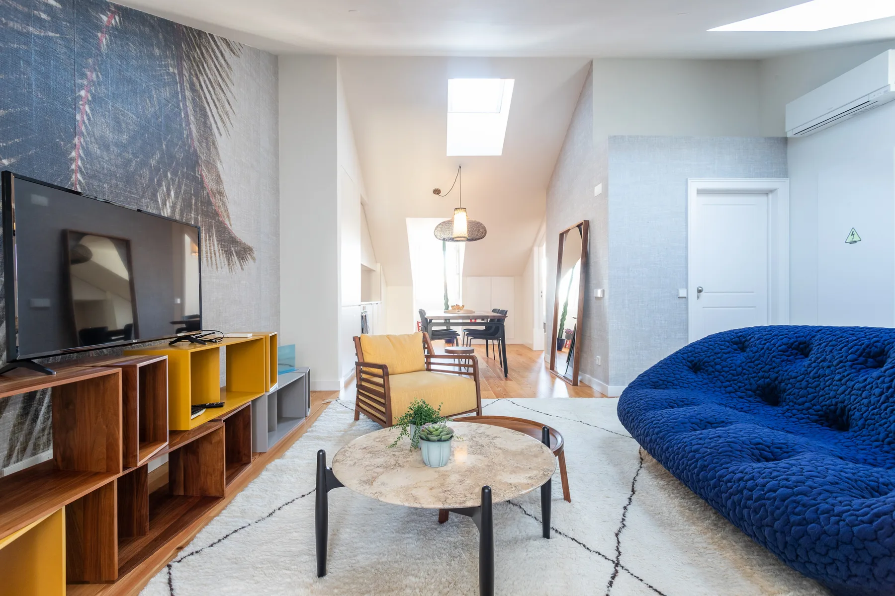 A bright living room with a television, coffee table, and blue seating.