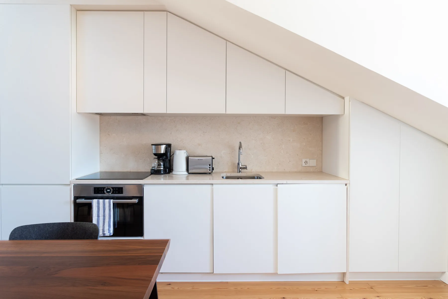 A compact kitchen with white cabinets, a countertop, and a wooden dining table.