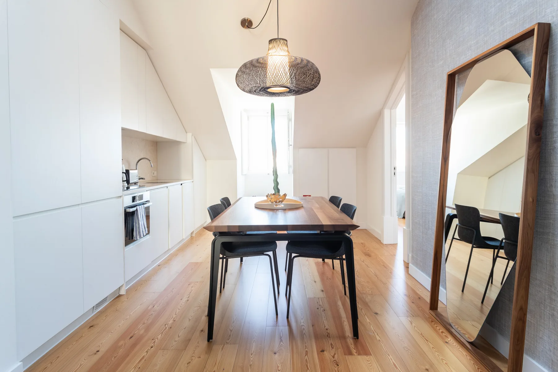 A dining area with a wooden table and a compact kitchen along the wall.