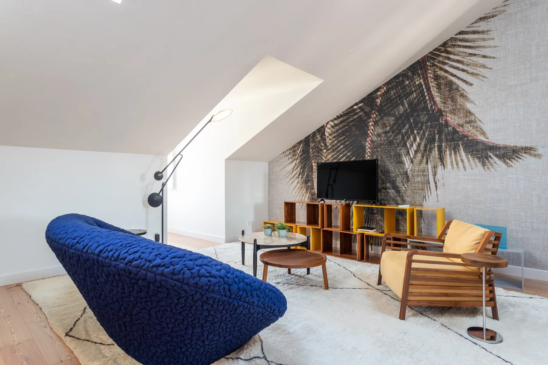 A bright living room features seating, a television, and a large palm mural.