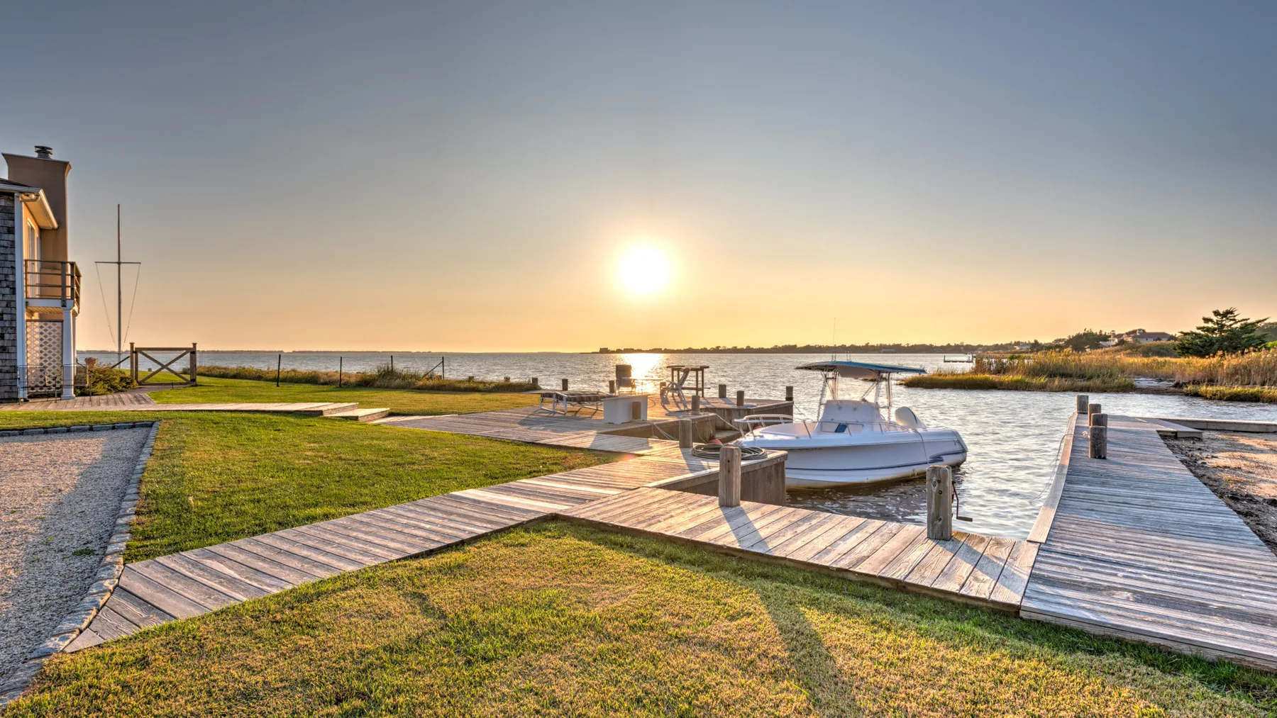 Un muelle junto al agua y una embarcación bordean la orilla cubierta de césped al atardecer.