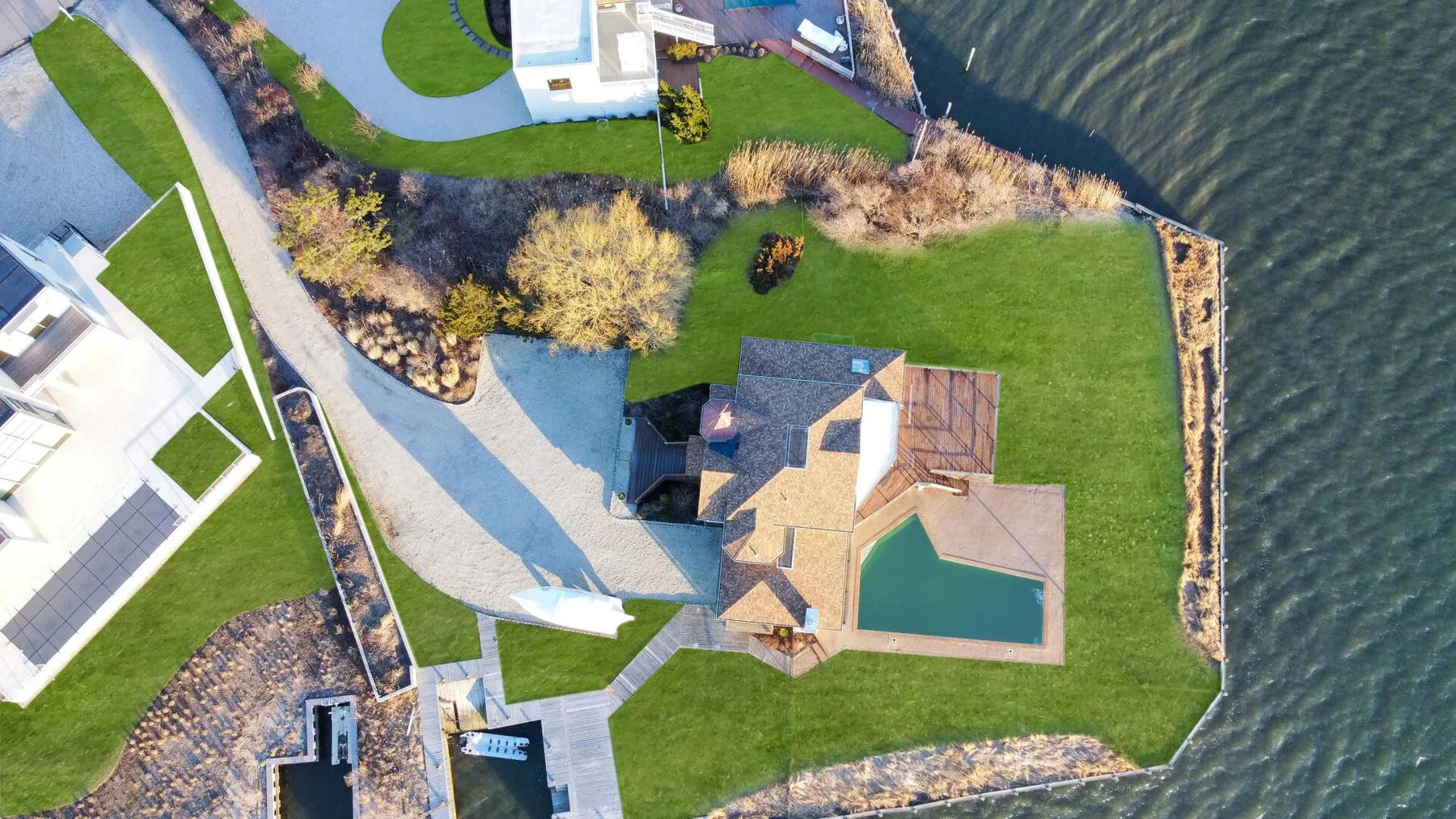 Vista aérea de una casa junto a un césped y una piscina cerca del agua.