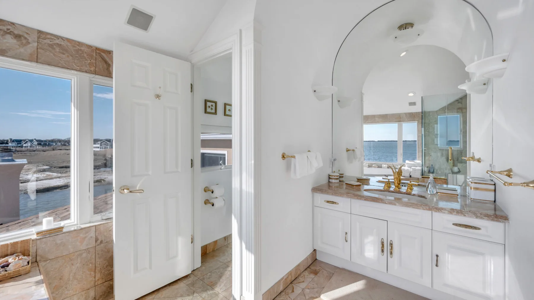 Un baño luminoso con tocador blanco, espejo grande y ventanas con vista al agua.