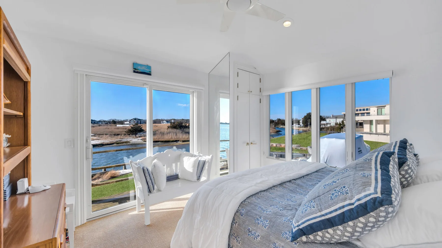 Un dormitorio luminoso con una cama junto a grandes ventanas con vista al agua.