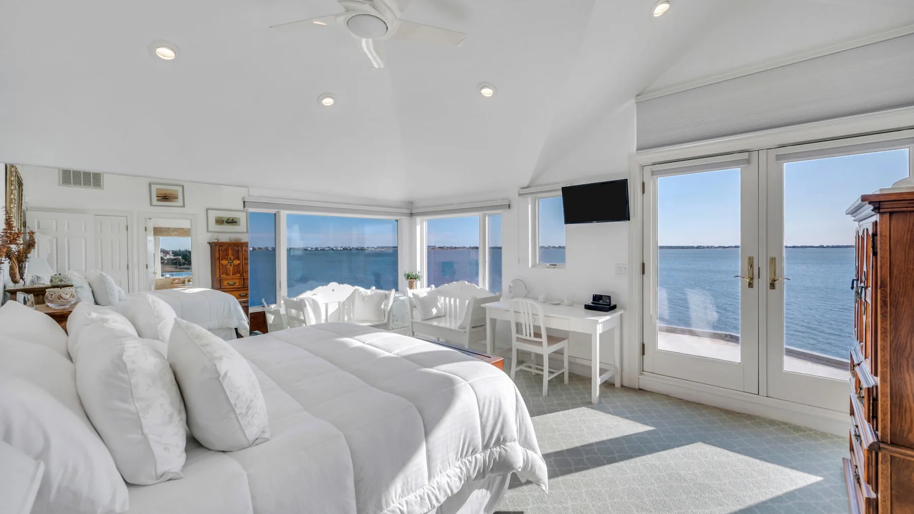 Un dormitorio luminoso con ropa de cama blanca, una pequeña mesa y vistas al agua.