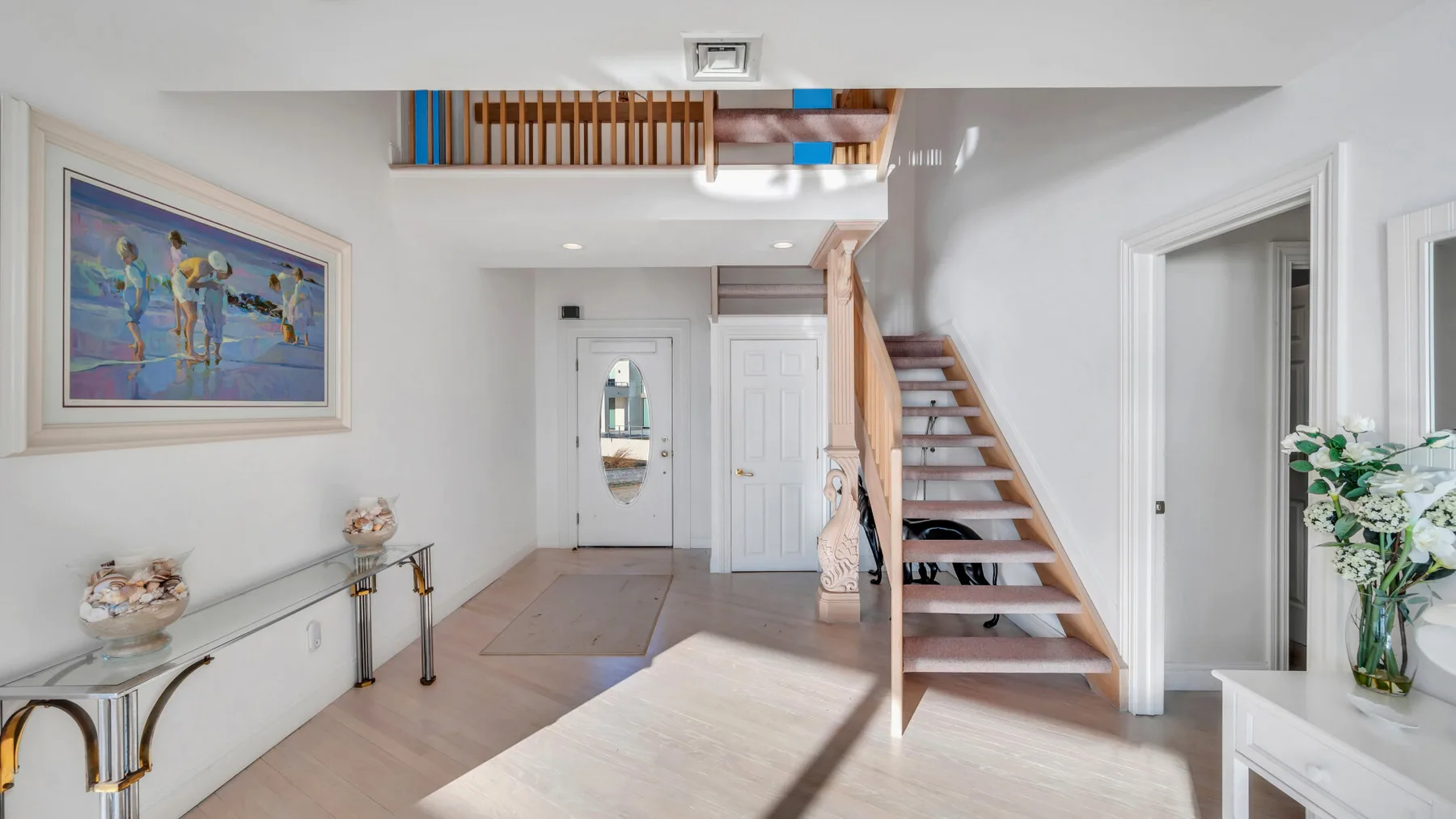 Un pasillo interior luminoso con una escalera y una obra enmarcada.