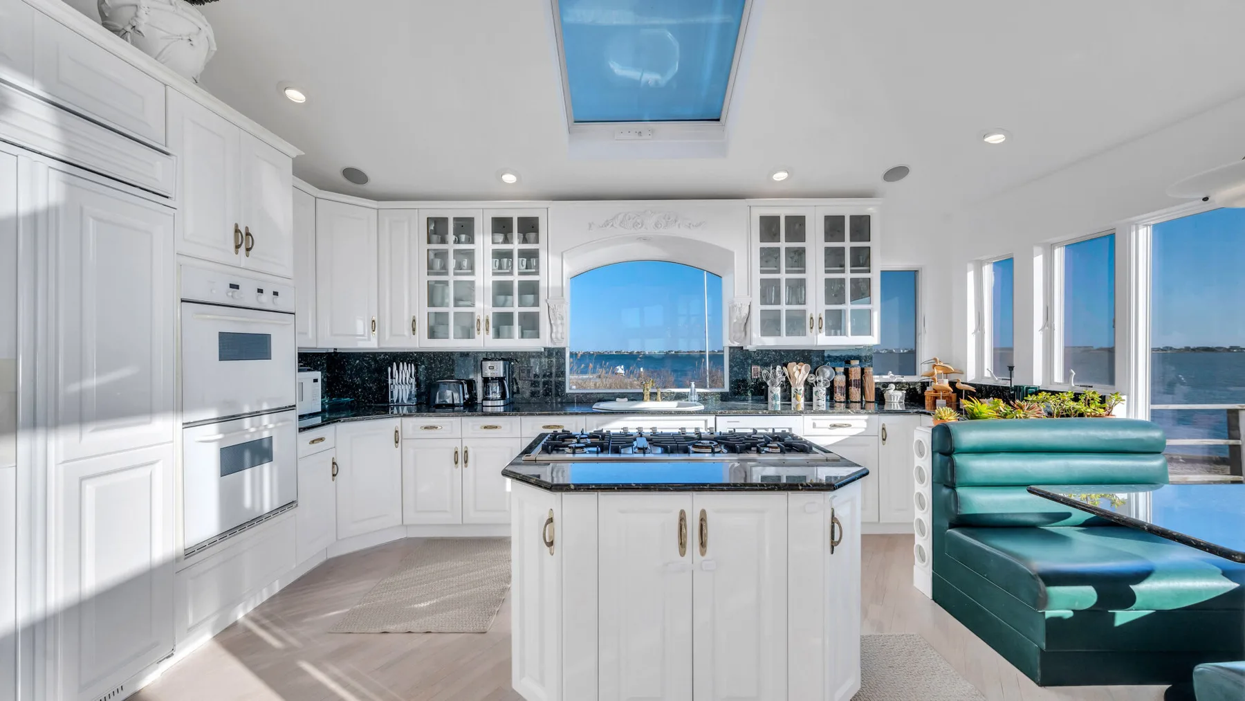 Una cocina luminosa con gabinetes blancos, una isla central y ventanas con vista al agua.