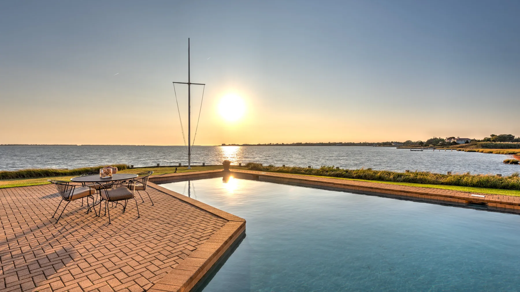Una piscina junto al agua y un patio pavimentado ofrecen vistas al atardecer.