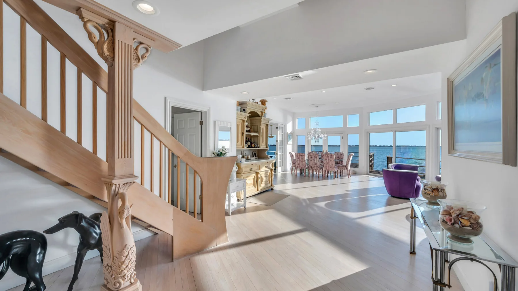 Un comedor y sala de estar luminosos con una escalera de madera y grandes ventanas.