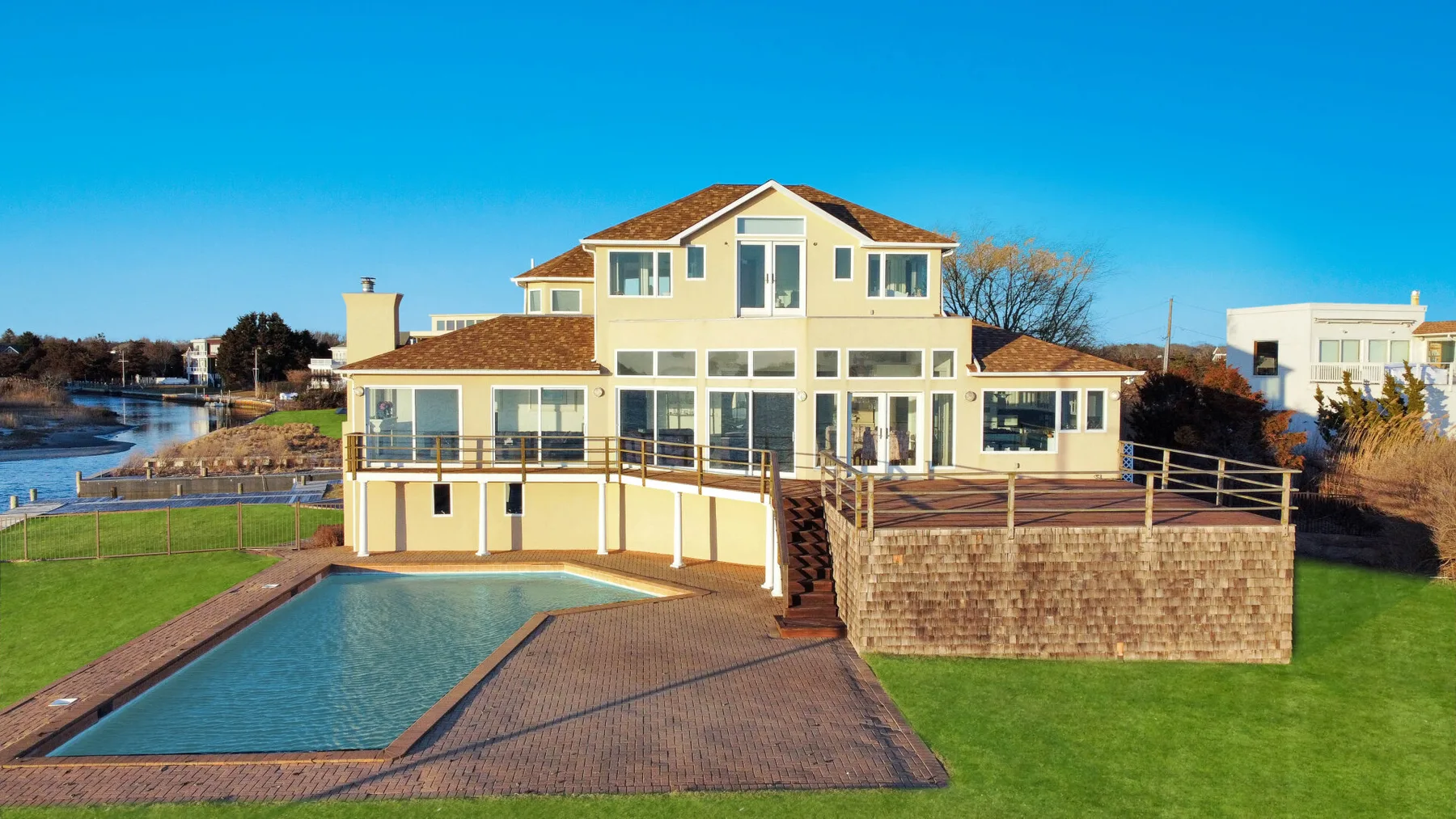 Una amplia casa junto al agua da a una piscina y una extensa terraza pavimentada.