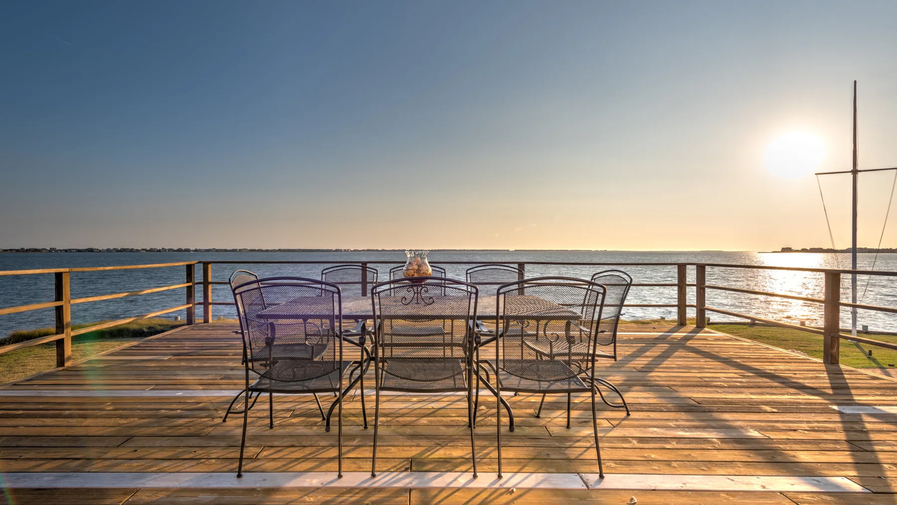 Una terraza junto al agua con asientos metálicos da a aguas tranquilas al atardecer.