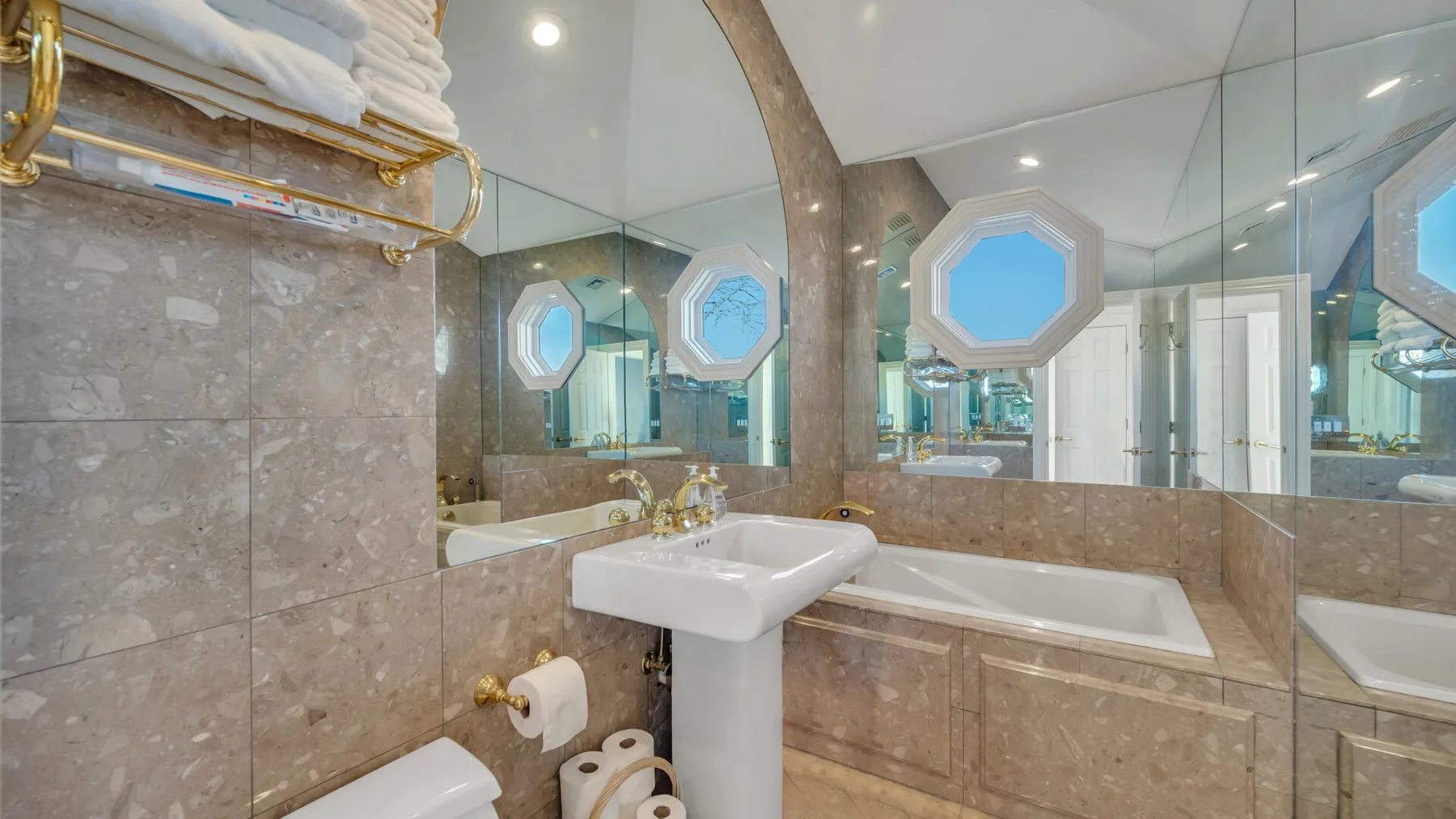 Un baño con lavabo blanco, bañera y paredes con espejos.