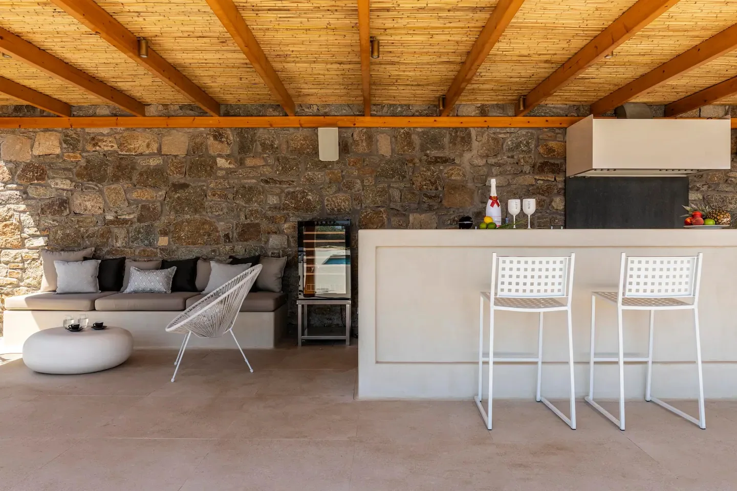 A covered outdoor lounge and bar area with seating and a stone wall.