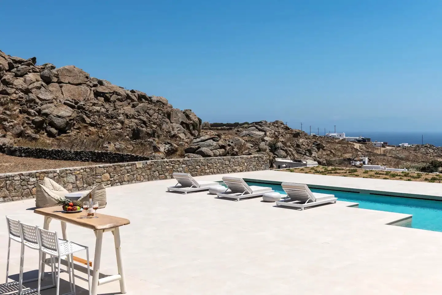 A sunlit pool terrace with loungers overlooks a rocky landscape.