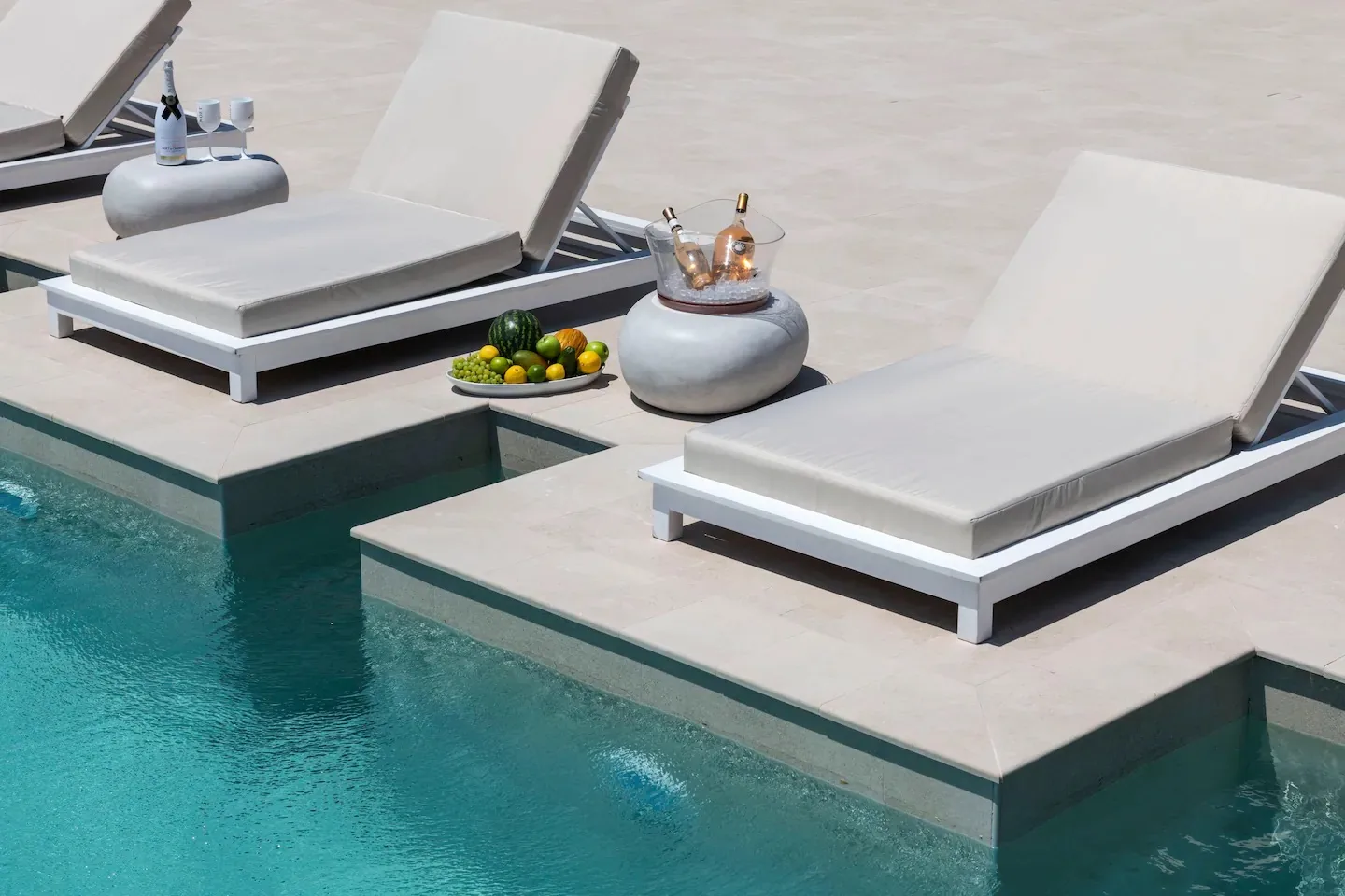 Poolside lounge chairs sit on raised platforms beside clear turquoise water.