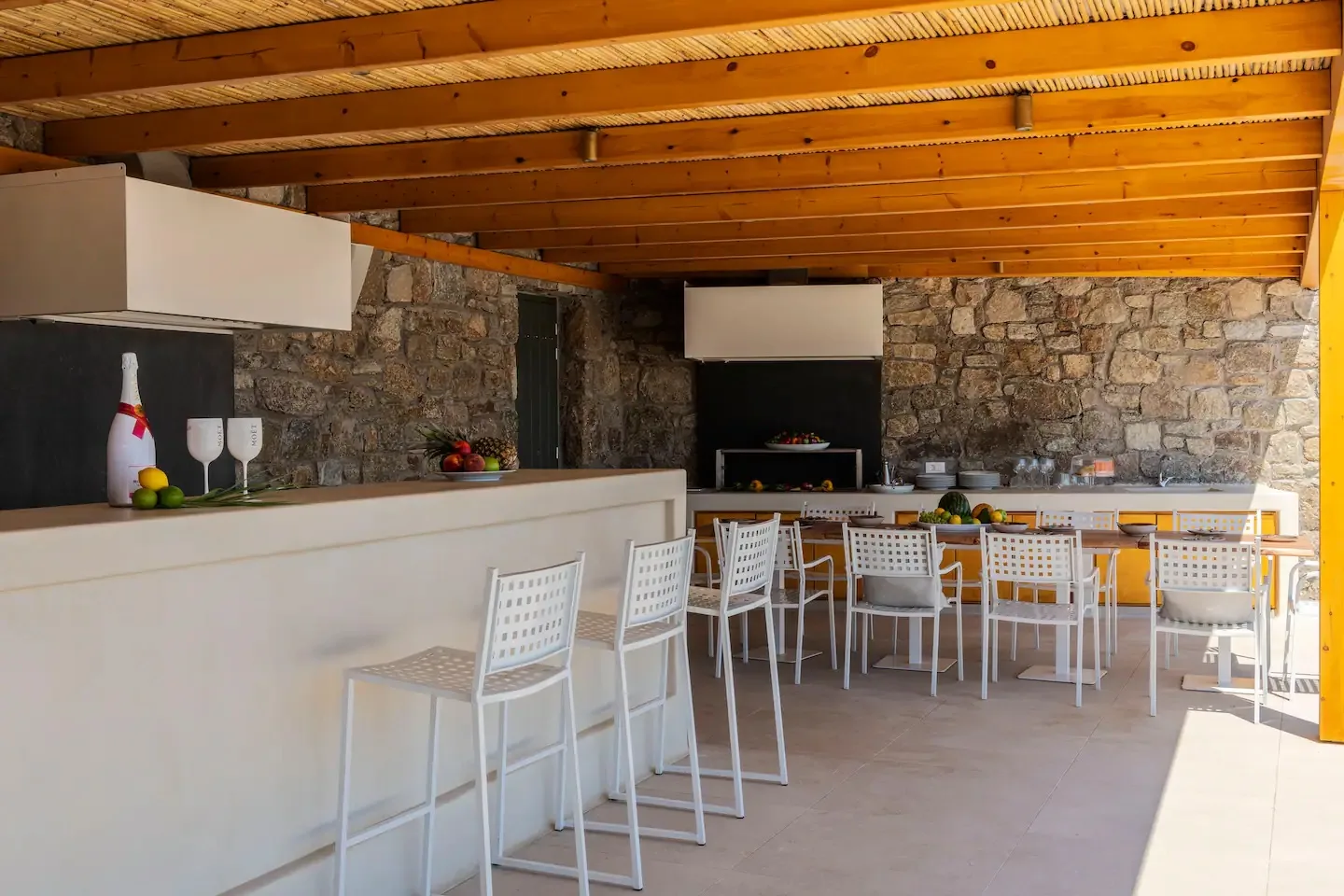 A covered outdoor dining area with a long table and stone walls.