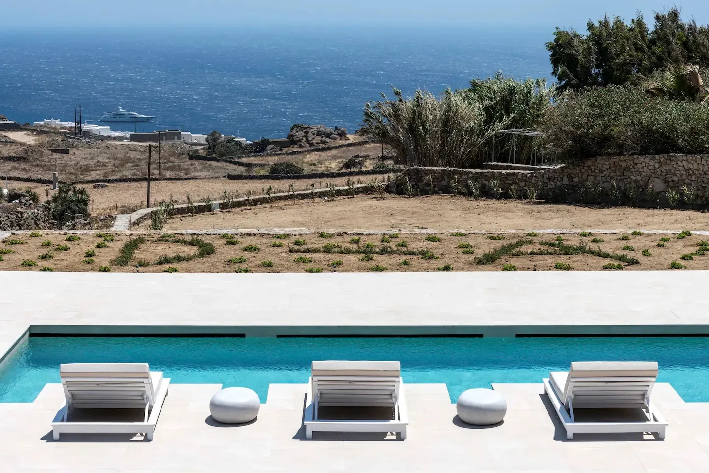 A swimming pool with lounge seating overlooks the sea.