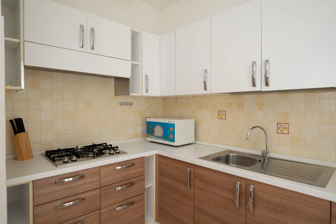 Una cocina con gabinetes blancos, cajones de madera, una estufa y un fregadero.
