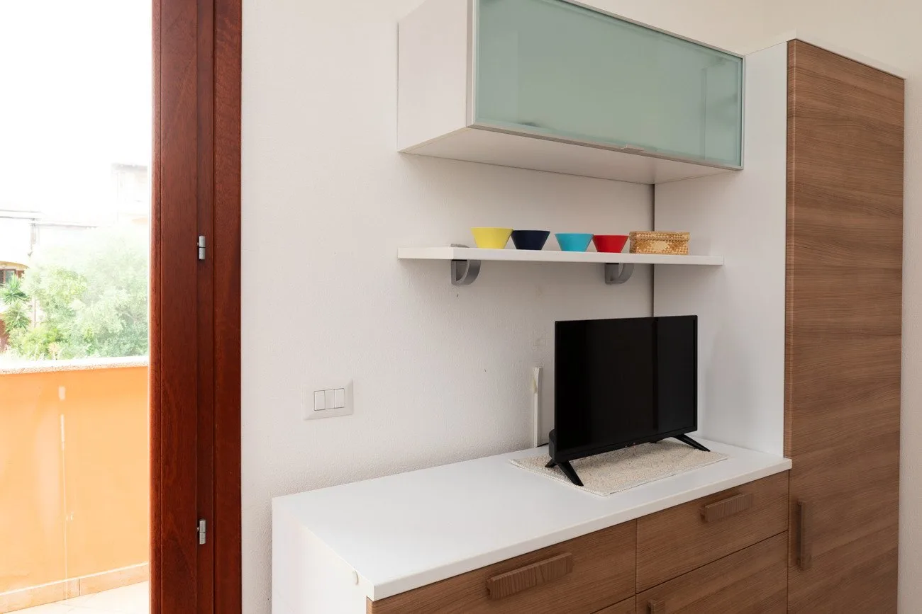 Una habitación moderna tiene un televisor sobre una encimera blanca junto a una puerta abierta al balcón.