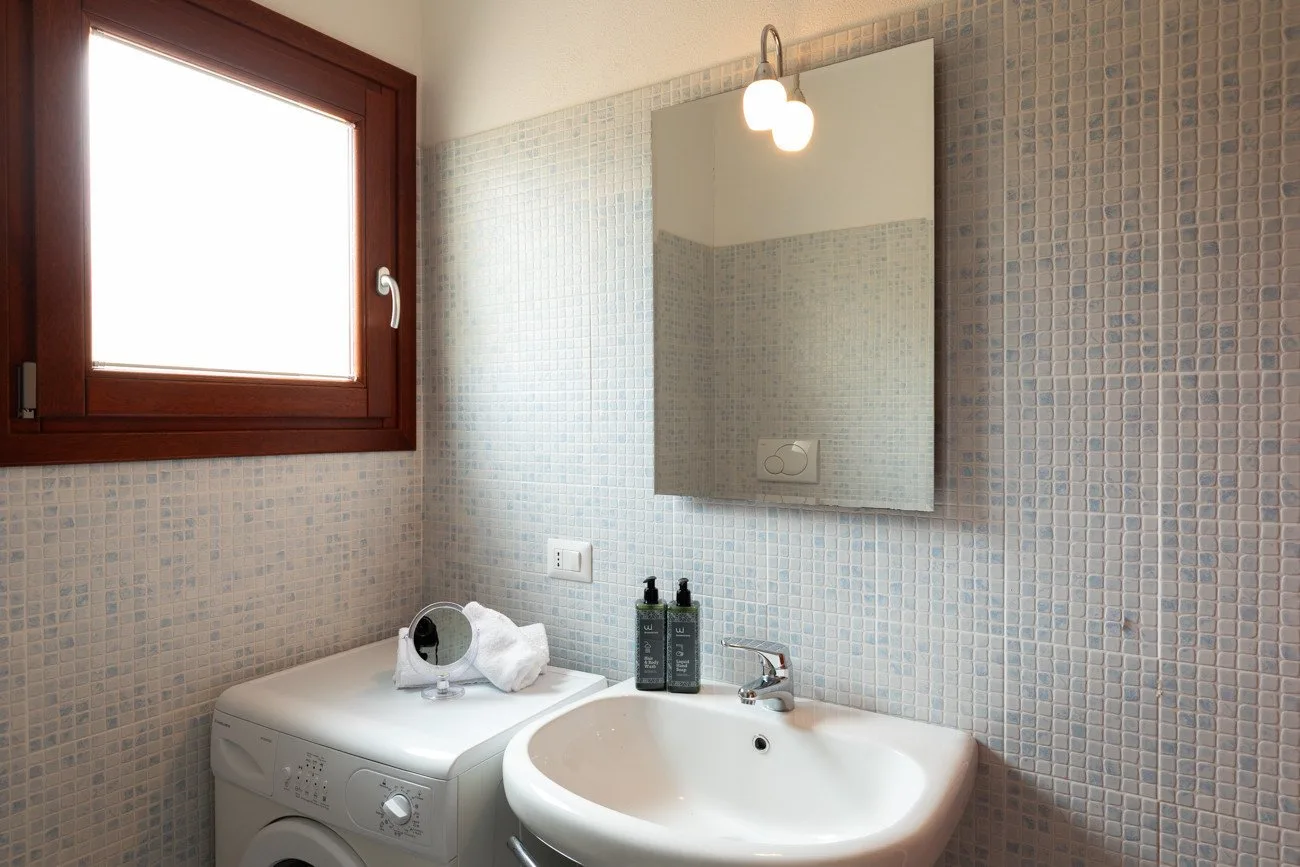 Baño con azulejos, lavabo, lavadora y ventana.
