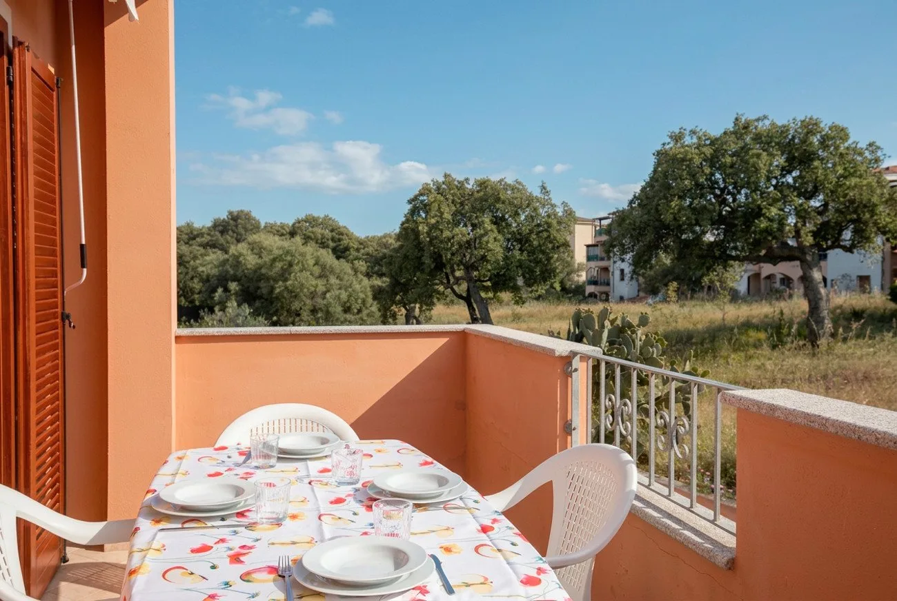 Una terraza exterior tiene una mesa puesta con platos junto a una barandilla.
