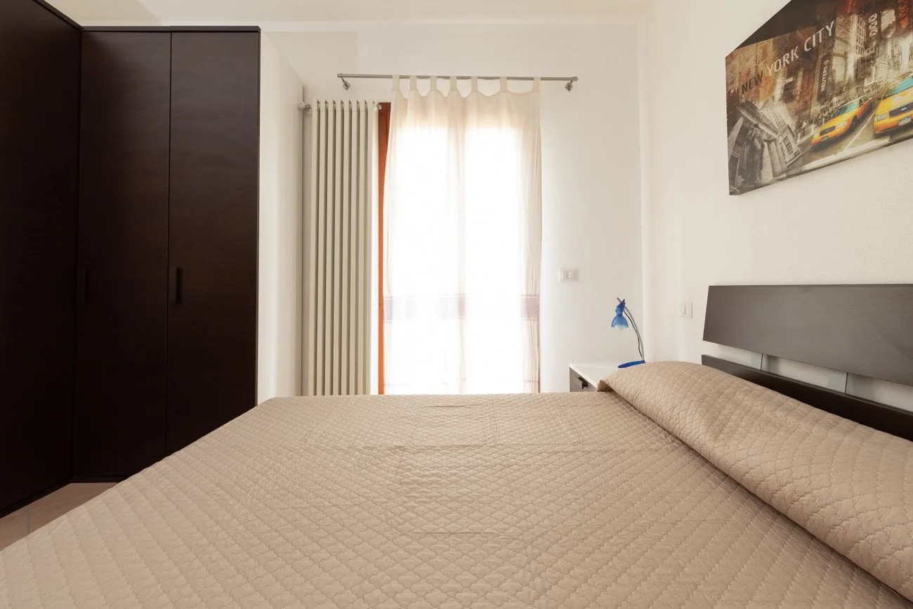 Un dormitorio con una cama grande, un armario oscuro y una ventana luminosa con cortinas.