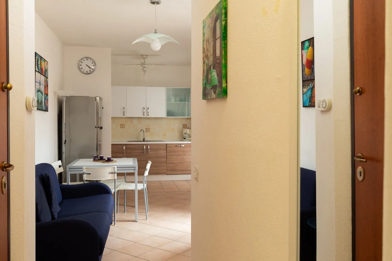 Se ve una cocina y un comedor al fondo del pasillo, con un sofá azul en primer plano.