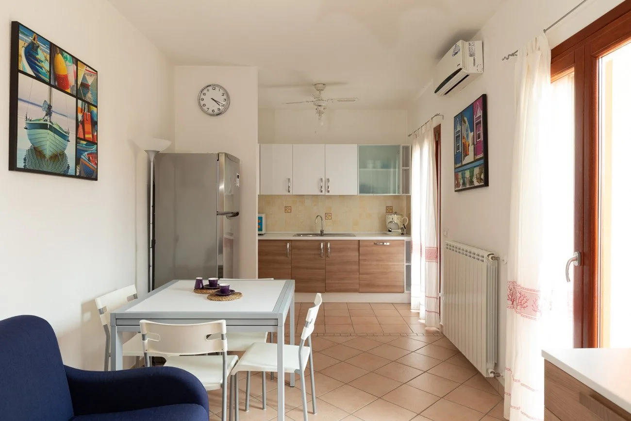 Un comedor se abre a una cocina, con una mesa junto a un refrigerador.