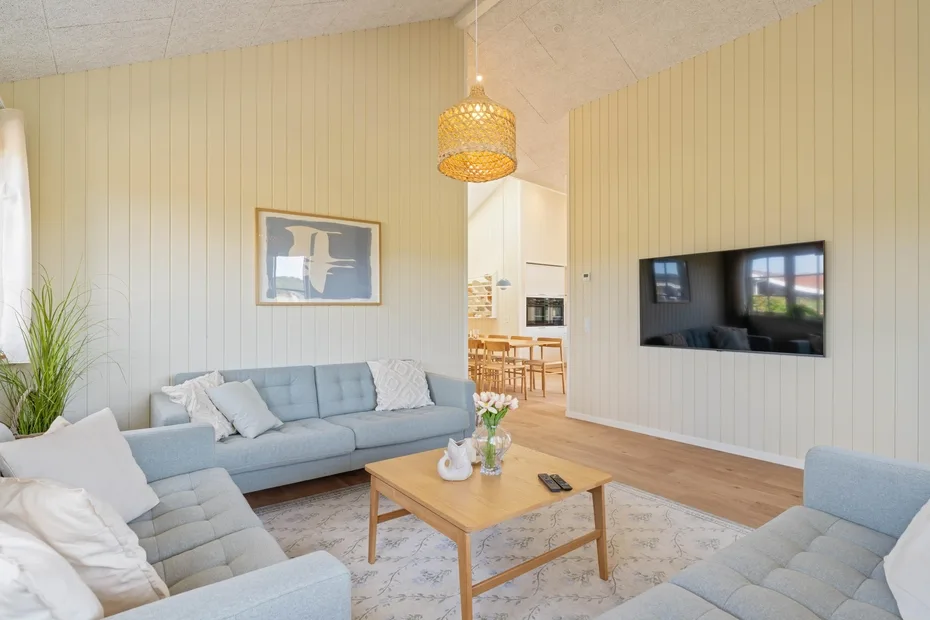 Una sala luminosa con asientos claros, una mesa de centro y un televisor en la pared.