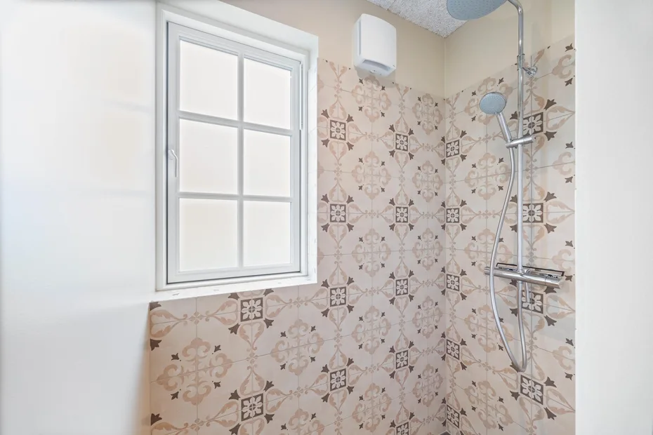 Un baño alicatado con una ventana y accesorios de ducha en la pared.
