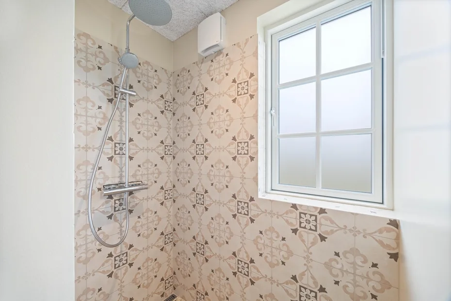 Zona de ducha con azulejos junto a una ventana grande.