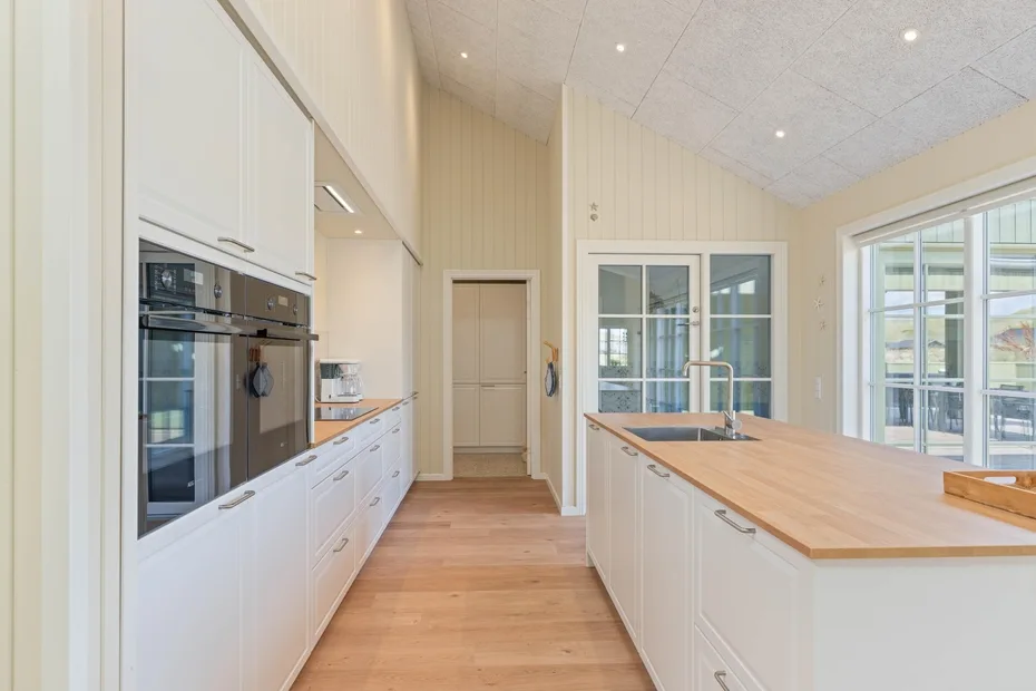 Una cocina luminosa con gabinetes blancos, una isla central y grandes ventanas.
