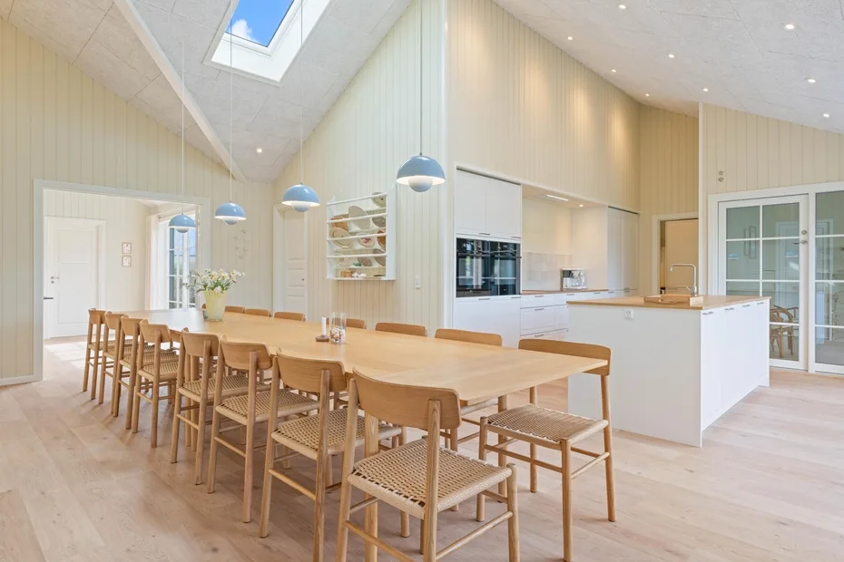 Un comedor luminoso con una larga mesa de madera junto a una cocina abierta.